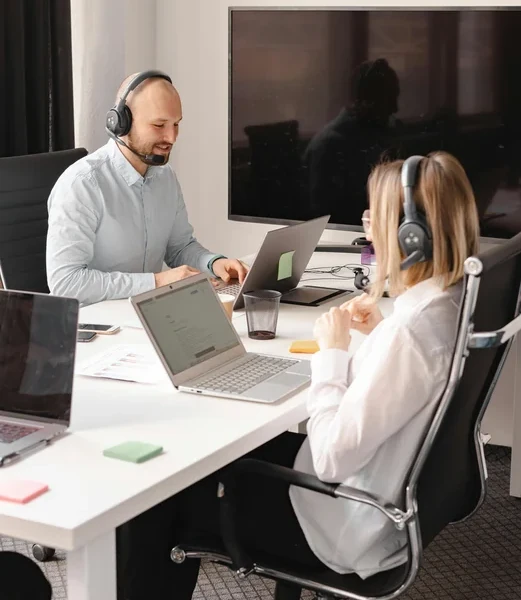 Zwei Mitarbeitende mit Headsets arbeiten im modernen Büro am Laptop und führen ein Meeting.